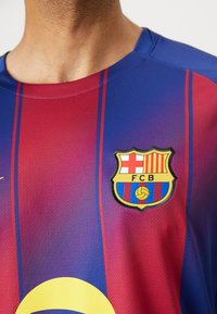 FC Barcelona dres u crvenoj i plavoj boji s okomitim prugama, s rundastim logom koji sadrži loptu i inicijale momčadi, izrađen od prozračnog materijala.