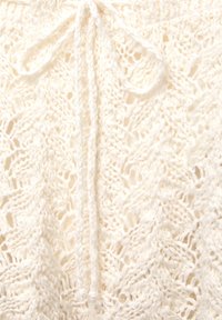 Knit cream-colored garment with a lace pattern, featuring a central tie detail. Textured design shows openwork and delicate stitching.
