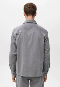 Camisa de pana gris con cuello, mangas largas y detalles de botones. Presenta una textura acanalada vertical y un ajuste relajado.