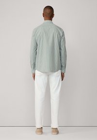 Camicia a scacchi verdi con colletto button-down, indossata sopra pantaloni bianchi, abbinata a calzature beige. Fit dritto e maniche lunghe.