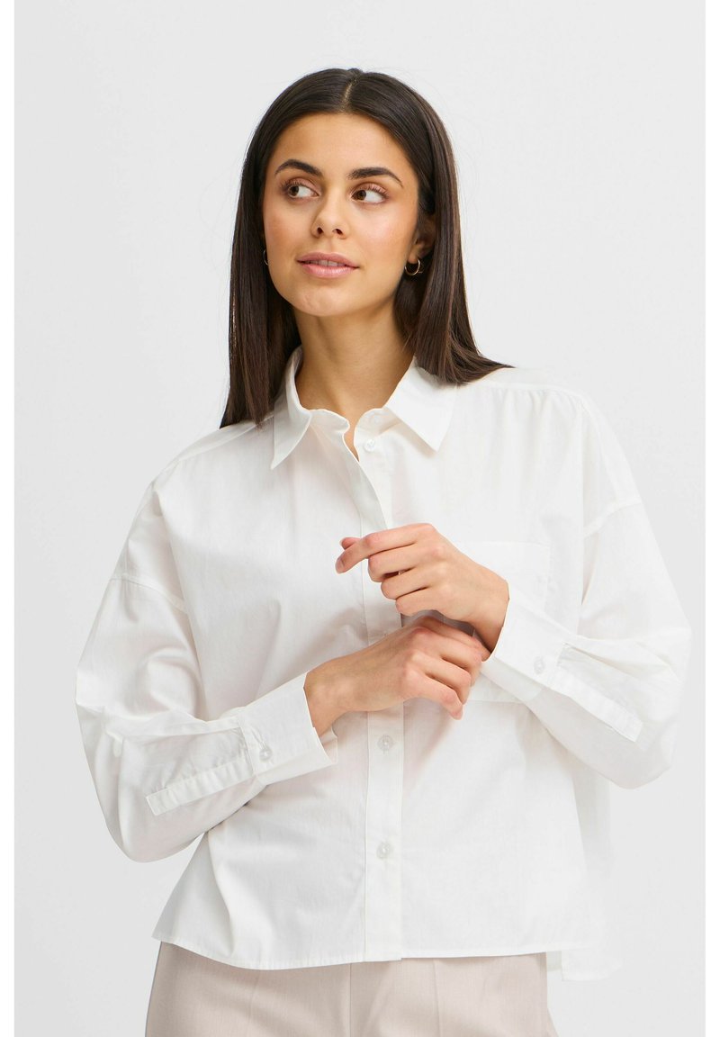 Camicia bianca con colletto a bottoni, dalla vestibilità rilassata, maniche lunghe, taschino singolo sul petto e una texture in cotone morbida. Taglio sartoriale con una finitura morbida.
