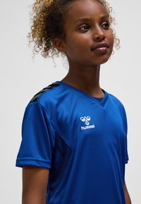 Blå träningsskjorta i slät, lätt tyg med korta ärmar, V-ringning och svarta randdetaljer på axlarna.