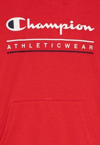 Sudadera roja con bolsillo canguro. Presenta el logo blanco de "Champion" y el texto "ATHLETICWEAR" en colores contrastantes. Textura suave.