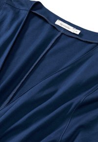 Haut pour femme bleu marine en tissu doux, doté d'un décolleté en V profond, de coutures subtiles et d'une étiquette intérieure cousue au niveau du col.