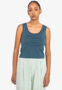 Tyrkis cropped tanktop lavet af ribbet stof, med en rund halsudskæring og subtil brandbroderi. Sat sammen med stribede, letvægtsbukser.