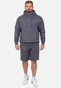 Grijze hoodie met trekkoorden en een voorzak, gecombineerd met bijpassende grijze shorts. Gemaakt met witte sneakers. Duurzame stof, casual pasvorm.