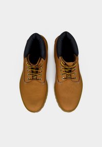 Bruine leren laarzen met een zwart gevoerde kraag, gele veters en een getextureerde rubberen zool. Voorzien van metalen oogjes en versterkte stiksels.