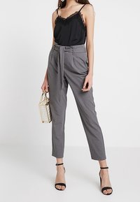 Zwarte cami-top met kantafwerking, gecombineerd met hoge grijze broek met een strikceintuur, slim fit en cropped lengte. Zwarte sandaaltjes met banden.