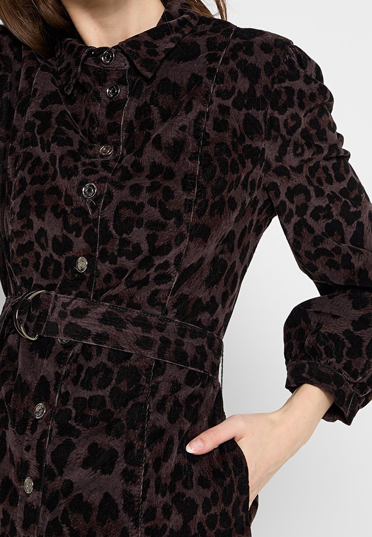 Abito camicia in velluto a coste con stampa leopardata in marrone scuro e nero, dotato di colletto, bottoni frontali, vita con cintura e maniche lunghe.