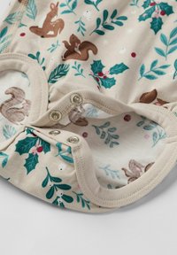 Puuvillainen haalari, jossa on vaalea tausta ja koristeltu oravien, lehtien ja holly-kuvioilla, pohjassa napitetut sulkemiset.