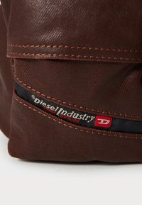 Brown fabric bag with visible stitching, logo tag reading "Diesel Industry," and a textured surface. Compact design with a flat profile.