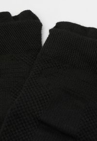 Svarta stickade tumlösa handskar med strukturerade mönster och ribbade muddar. Materialet verkar mjukt och elastiskt med detaljerad sömnad.