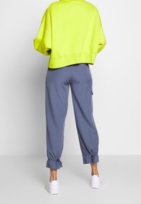 Grön kort sweatshirt med lösa ärmar, matchad med blå tapered byxor med elastiska nederkanter och sidofickor. Vita sneakers fulländar stilen.