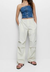 Denim-strapless-Top mit vorderseitigen Knöpfen, kombiniert mit lockeren cremefarbenen Hosen mit Taschen und gerafften Details. Dazu werden pinke Sandalen getragen.