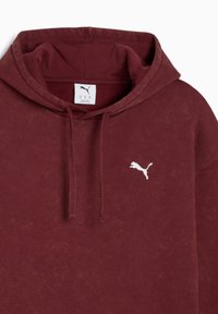 Bordeaux hoodie van textiel. Heeft een wit Puma-logo op de borst en koordjes bij de capuchon.