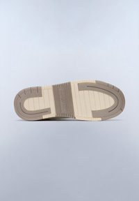 Suola di una sneaker realizzata in materiale gommoso beige con scanalature testurizzate e un dettaglio centrale con logo. Forma piatta e curvata con bordi a contrasto.