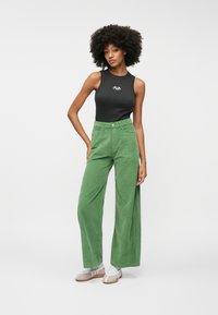 Green corduroy wide-leg pants with a high waist, paired with a black sleeveless top featuring a small logo at the chest. White and pink shoes.