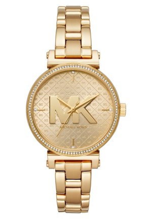 Montre-bracelet Michael Kors ton or avec grand logo MK sur le cadran, lunette ornée de cristaux et bracelet en métal à maillons.