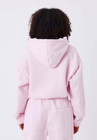 Hoodie rose clair avec capuche, offrant une coupe décontractée et des détails cousus. Tissu doux avec des poignets côtelés et un pantalon de jogging assorti.