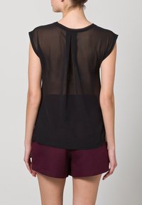Black sheer short-sleeve top with a split back design, paired with maroon shorts. The fabric appears lightweight and semi-transparent.