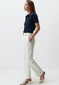 Polo côtelé marine avec col, associé à un pantalon blanc à jambe droite. Les chaussures sont des escarpins nude à bout pointu. Design simple et épuré, sans motifs.