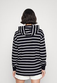 Marineblauwe en witte gestreepte hoodie met een voorste kangoeroezak. Voorzien van een gevoerde capuchon en ribgebreide manchetten. Zachte stof met een ontspannen pasvorm.