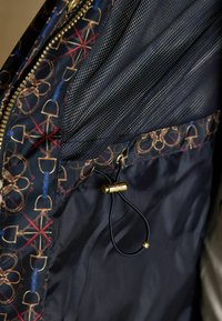 Jūras jaka ar iekšpusi, kas izgatavota no tīkla auduma, ar zelta apdari un krustotu instrumentu rakstu. Regulējams vads ar zelta pogu.