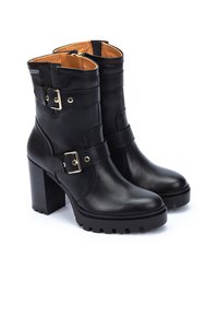 Botas de cuero negro hasta el tobillo con un tacón robusto, con dos correas con hebillas doradas y un sutil logo en relieve. Suela texturizada para mayor agarre.