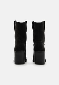 Czarne zamszowe botki za kostkę z grubym kwadratowym obcasem. Posiadają miękką teksturę i pętle z tyłu ułatwiające zakładanie. Minimalistyczny design.