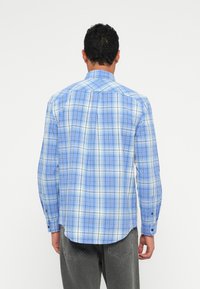 Ανοιχτού μπλε καρό πουκάμισο με πουκάμισο με κουμπιά, μακριά μανίκια και ελαφρώς καμπυλωτό στρίφωμα. Διαθέτει μικρούς κουμπίδες στις μανσέτες.