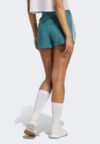 Türkise Sportshorts mit weißen Seitestreifen, enger Passform und glatter Textur. Kombiniert mit weißen knielangen Socken und Sneakers.