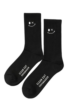 Calzini a costine neri con il testo bianco "CLEAN CUT COPENHAGEN" sulle suole e una piccola faccina sorridente ammiccante ricamata vicino alla parte superiore.