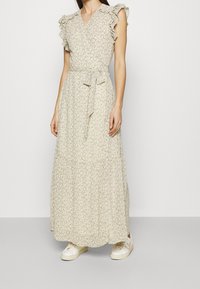 Vaaleankermanvärinen kukkakuosinen maksimekko, jossa röyhelöhihat, vyötärönauha ja kerroksittainen hame. Yhdistetty valkoisiin lenkkareihin, joissa on vaaleanpunainen yksityiskohta.