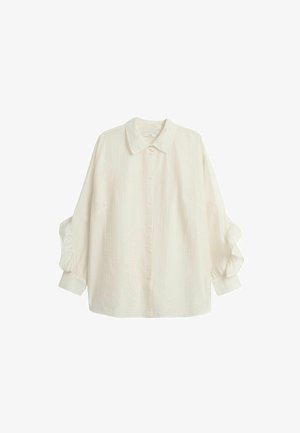 Biała, długa koszula z długim rękawem, zapinana na guziki, uszyta z fakturowanej tkaniny. Posiada klasyczny kołnierz oraz marszczone detale przy rękawach.