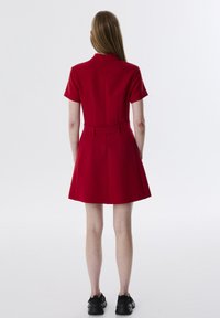 Abito rosso con maniche corte, in vita aderente e gonna svasata. Presenta un collo alto e una vita con cintura. Tessuto liscio e dettagli minimi.