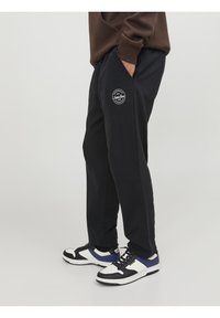 Černé tepláky z měkké látky, s bočními kapsami a kulatou nášivkou na levém stehně. Kombinované s černo-bílými teniskami.