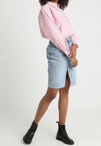 Roze en witte gestreepte overhemd met losse mouwen, gecombineerd met een lichtblauwe denim rok met een voorzijde-split. Zwarte enkellaarzen.