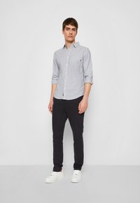 Gestreifte Button-Down-Hemd aus hellblauem und weißem Baumwollstoff, kombiniert mit einer dunklen, schmalen Hose und weißen Sneakers. Einfaches Design mit Brusttasche.