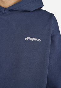 Navy blue hooded sweatshirt with white cursive "PEGADOR" logo embroidered on the chest.
