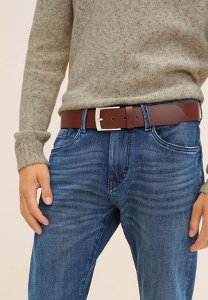 Brown leather belt with a silver rectangular buckle, worn over blue jeans. The sweater is light gray, knitted, and features a crew neck.