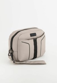 Beige nylon toilettaske med sort lynlås og rem. Har en frontlomme med sorte accentlinjer og polstrede sider for struktur.