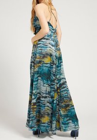 Robe maxi en bleu-vert avec un motif en vagues jaune et noir. Dotée de fines bretelles et d'un dos légèrement ouvert. Tissu fluide et design long jusqu'au sol.