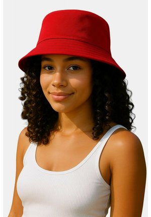 Red bucket hat in a soft fabric with a wide brim, worn by a person with curly hair. The background is plain white.