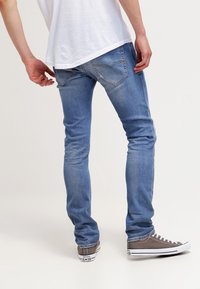 Jeans de denim azul claro con un diseño ajustado, bolsillos traseros visibles y un ligero desvanecimiento. Combinados con zapatillas grises con suelas blancas.
