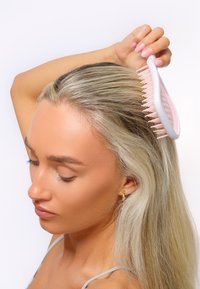 Rosa kam med breda och fina tänder hålls i en hand och kammar rakt, långt blont hår. Vit bakgrund, fokus på skötsel.