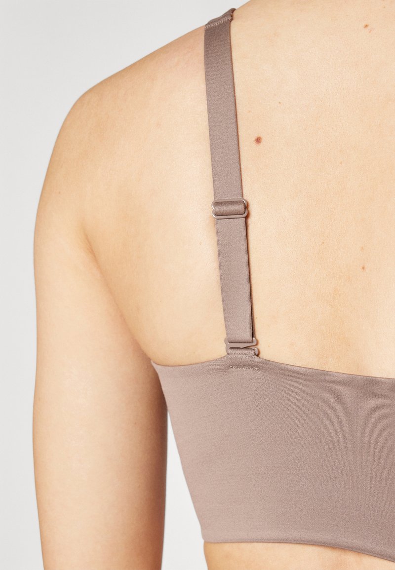 Bra aus braunem Stoff mit verstellbaren Trägern und einem Metallverschluss hinten. Glatte Textur mit schlichtem Design und ohne sichtbare Muster.