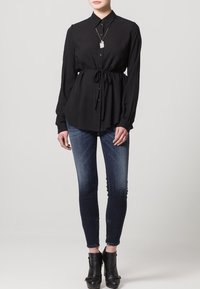 Svart långärmad blus med knyt i midjan, knäppning framtill och krage, kombinerad med mörkblå slim fit jeans och svarta ankelstövlar.