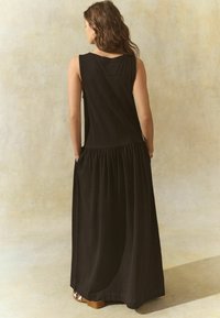 Robe maxi noire sans manches avec une jupe plissée et fluide, dotée de poches latérales, présentant un col arrondi et une coupe décontractée.