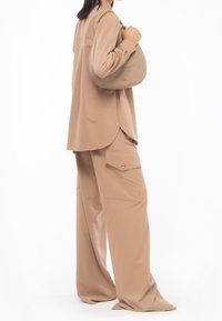Femme portant un pantalon cargo large beige et un haut à manches longues assorti, tenant un sac à main en cuir taupe avec une bandoulière en chaîne dorée sur l'épaule.