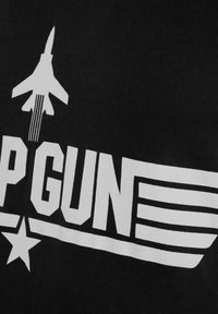 Mustakangas sisältää valkoisen graafisen kuvaston, jossa on suihkuhävittäjä ja teksti "TOP GUN" viivoineen ja tähdellä, mikä luo rohkean visuaalisen ilmaisun.